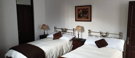 Une chambre avec deux lits, chacun doté d’une tête de lit en bois, de draps blancs et de plaids marron. On y trouve des tables de chevet avec des lampes et un tableau encadré au mur.
