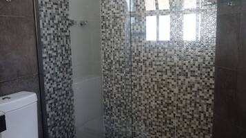 A bathroom with a toilet, a shower with a glass door, and tiled walls.