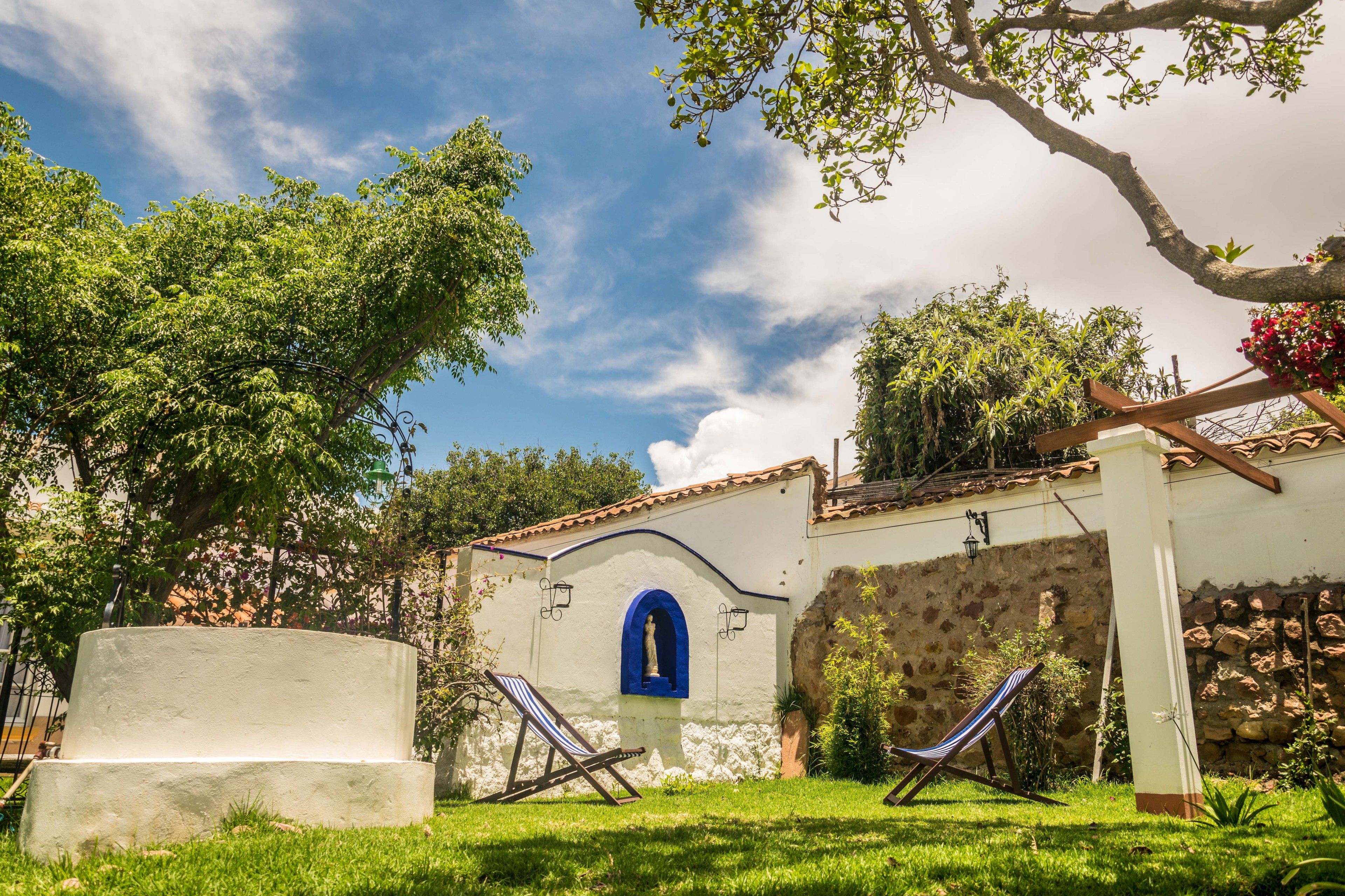 A white building with a blue arched window and a stone wall. There are two lounge chairs in the front yard.