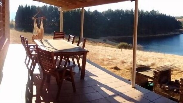 Un espace extérieur abrité, aménagé avec des sièges, et offrant une vue sur un lac et les collines environnantes.