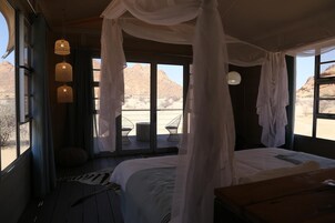 Un dormitorio con cama, cortinas y vistas al paisaje desértico.