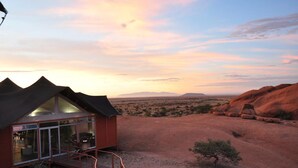 A modern building with a glass facade, situated in a desert landscape with red rock formations and a sunset sky. - Spitzkoppen Lodge (Usakos)