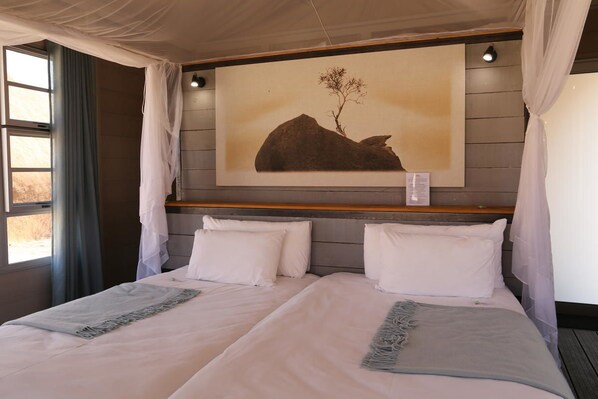 A double bed with a headboard, a window with curtains, and a wall-mounted artwork of a tree and rock. - Spitzkoppen Lodge (Usakos)