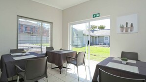 A conference room with tables and chairs, a large window with blinds, and a view of a building outside. - Eagle Cove (Randburg)
