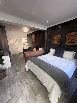 A bedroom with a large bed, a bedside table, a chair, and a desk. - Relaxed City Living (Gqeberha (Port Elizabeth))