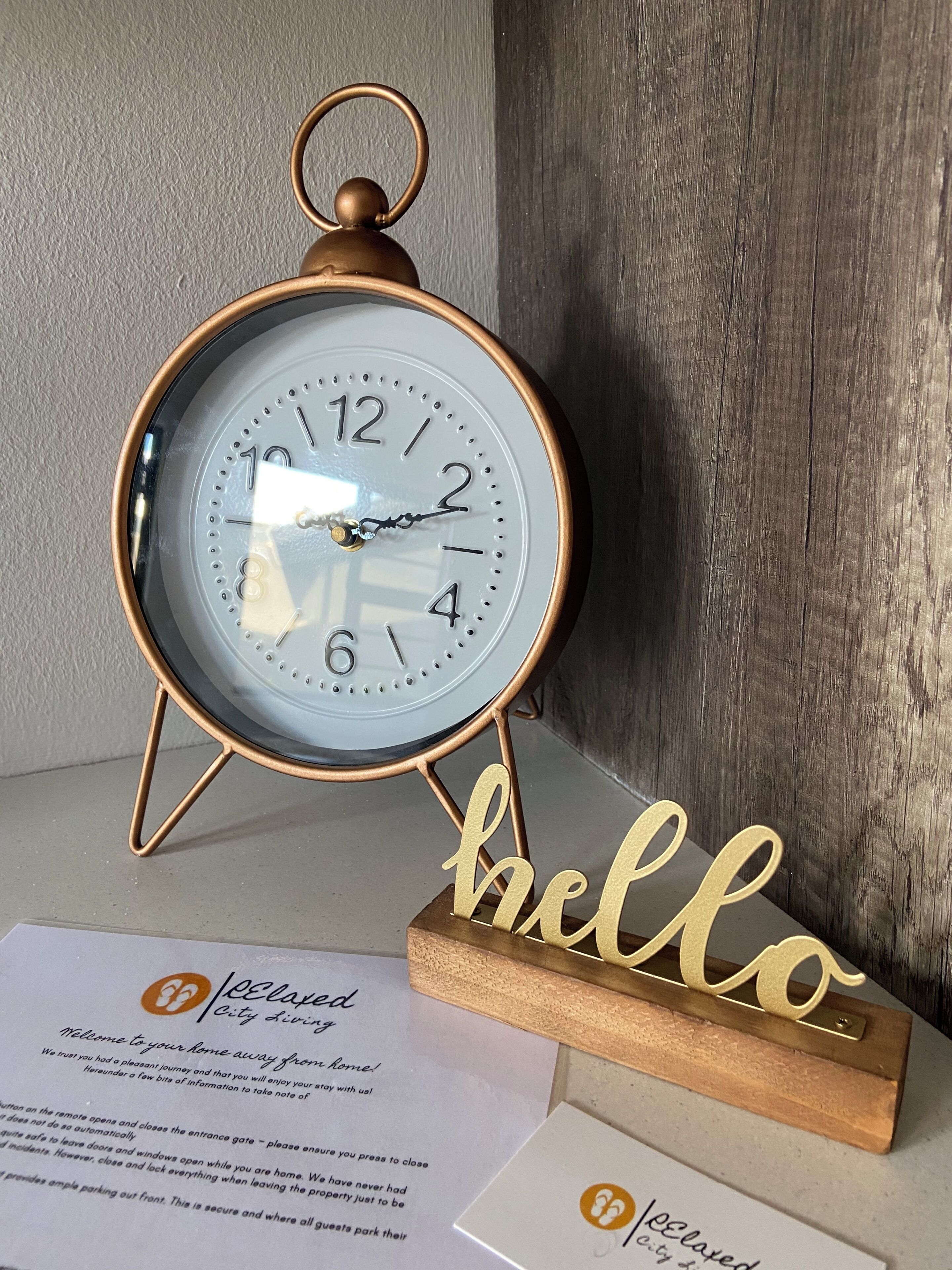 Un reloj de pared con detalles en latón y un cartel que dice 'hello' debajo.