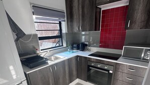 Una cocina moderna con armarios grises, un salpicadero rojo y un horno empotrado.