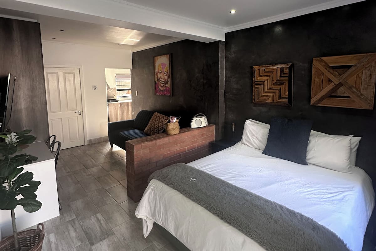 A modern bedroom with a large bed, a small sofa, a TV, and a dining area.