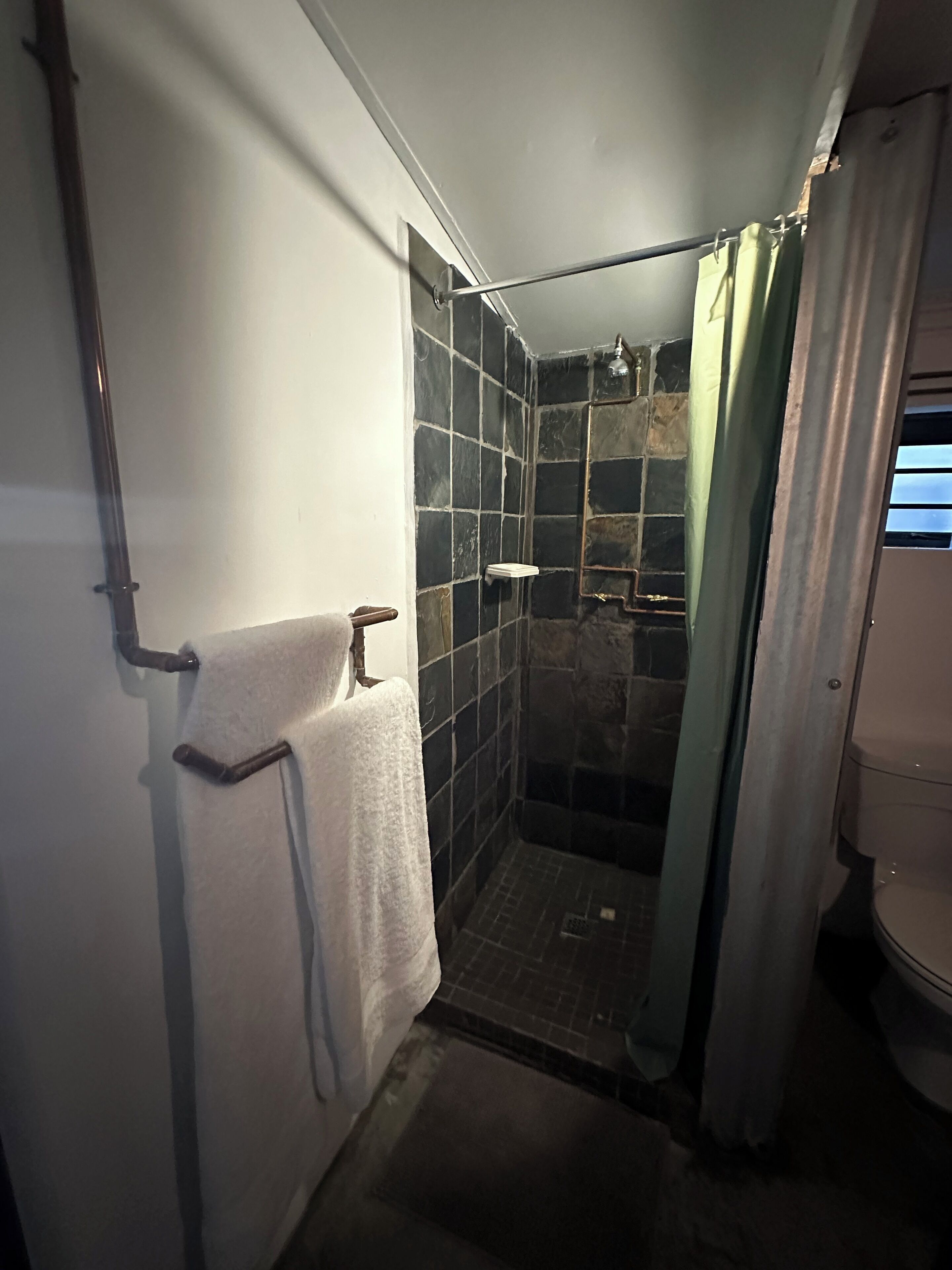 Un espacio de ducha pequeño con azulejos, una puerta de cristal, un perchero y un cabezal de ducha.