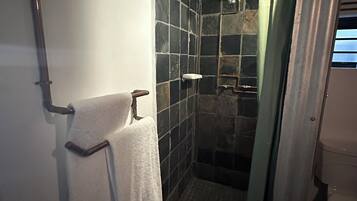 Un espacio de ducha pequeño con azulejos, una puerta de cristal, un perchero y un cabezal de ducha.