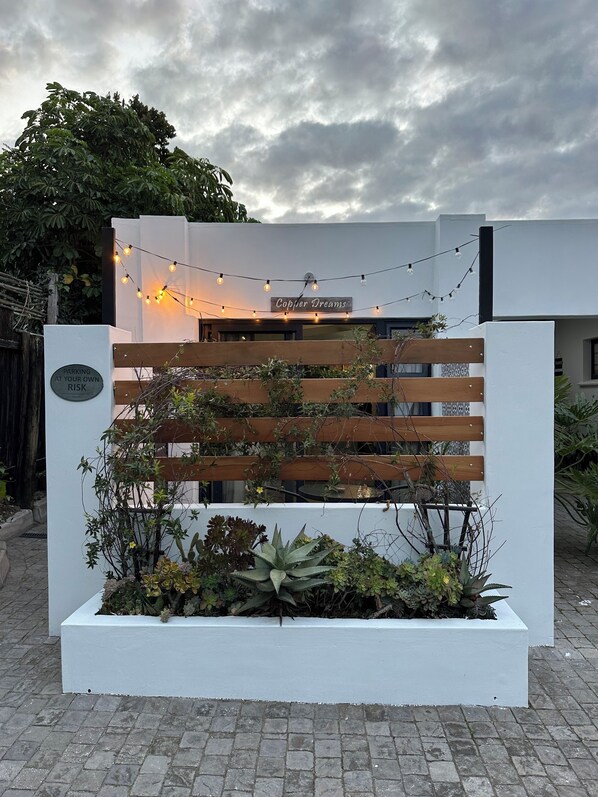 A modern building entrance with a wooden slatted gate, a sign reading "Copjier Dreams," and string lights above. - Relaxed City Living (Gqeberha (Port Elizabeth))