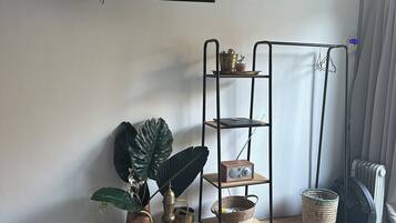 Una sala de estar con una televisión de pantalla plana montada en la pared, un mueble de metal con objetos decorativos, una planta grande y una alfombra tejida en el suelo.