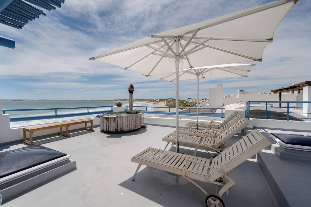 A rooftop terrace with lounge chairs, umbrellas, and a view of the sea.