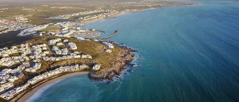 Vista aérea de una zona costera con edificios residenciales, un puerto deportivo y una costa curvada.