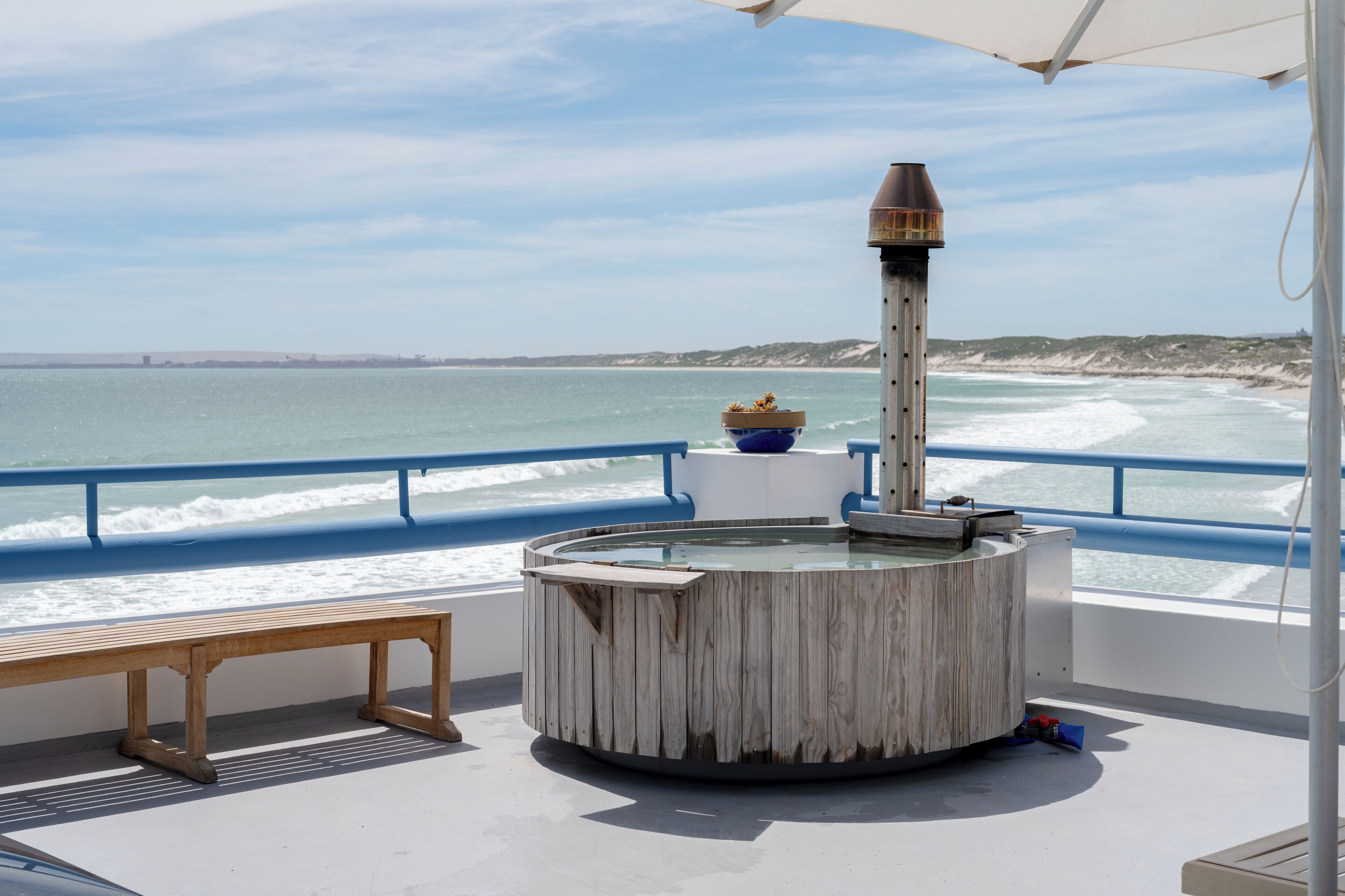A circular wooden structure with a chimney, a bench, and a railing overlooking the sea.