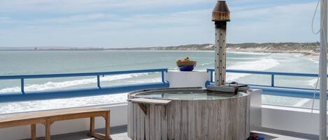 A circular wooden structure with a chimney, a bench, and a railing overlooking the sea.