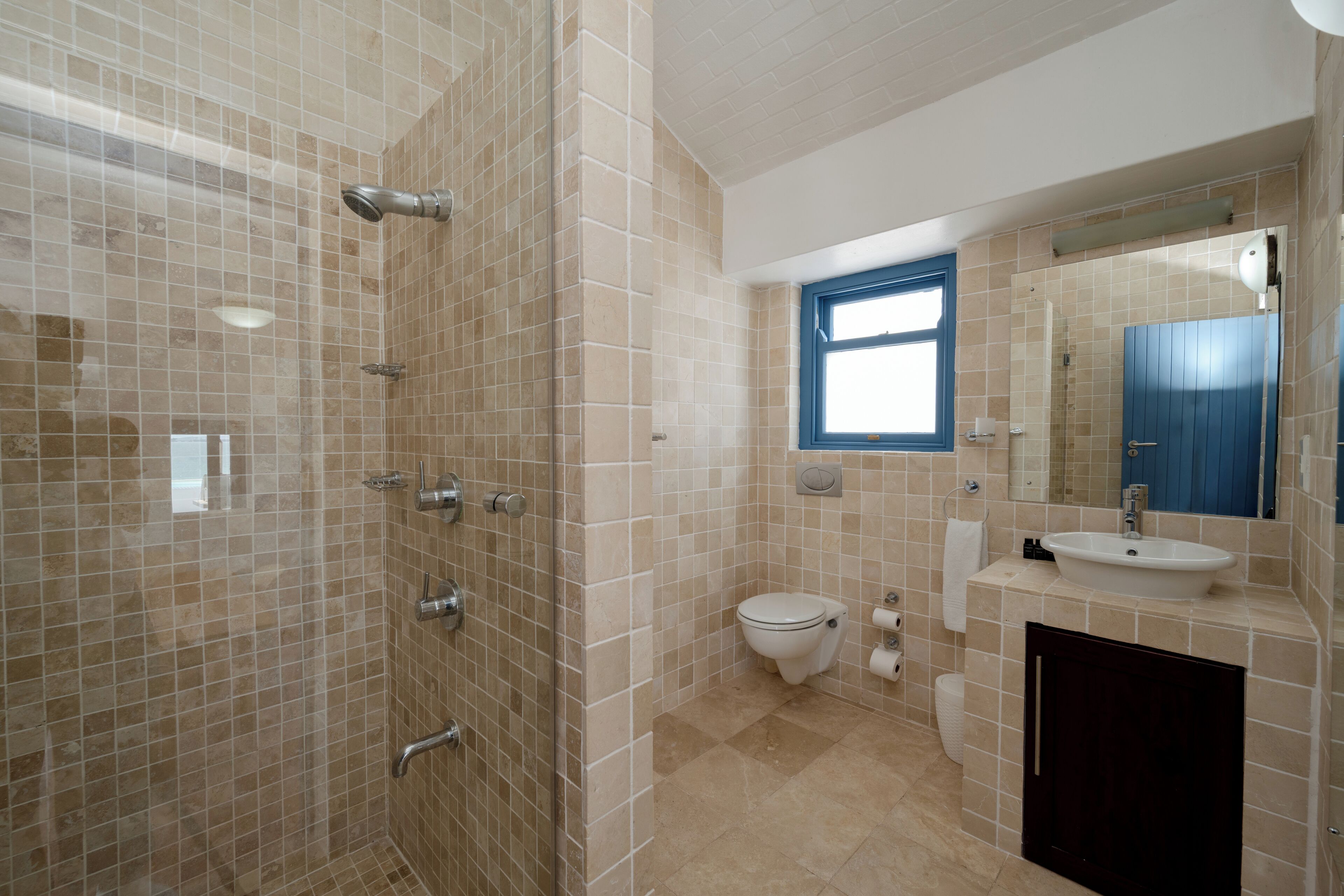 Un bagno con pareti piastrellate color beige, un water bianco, un lavandino e una doccia.