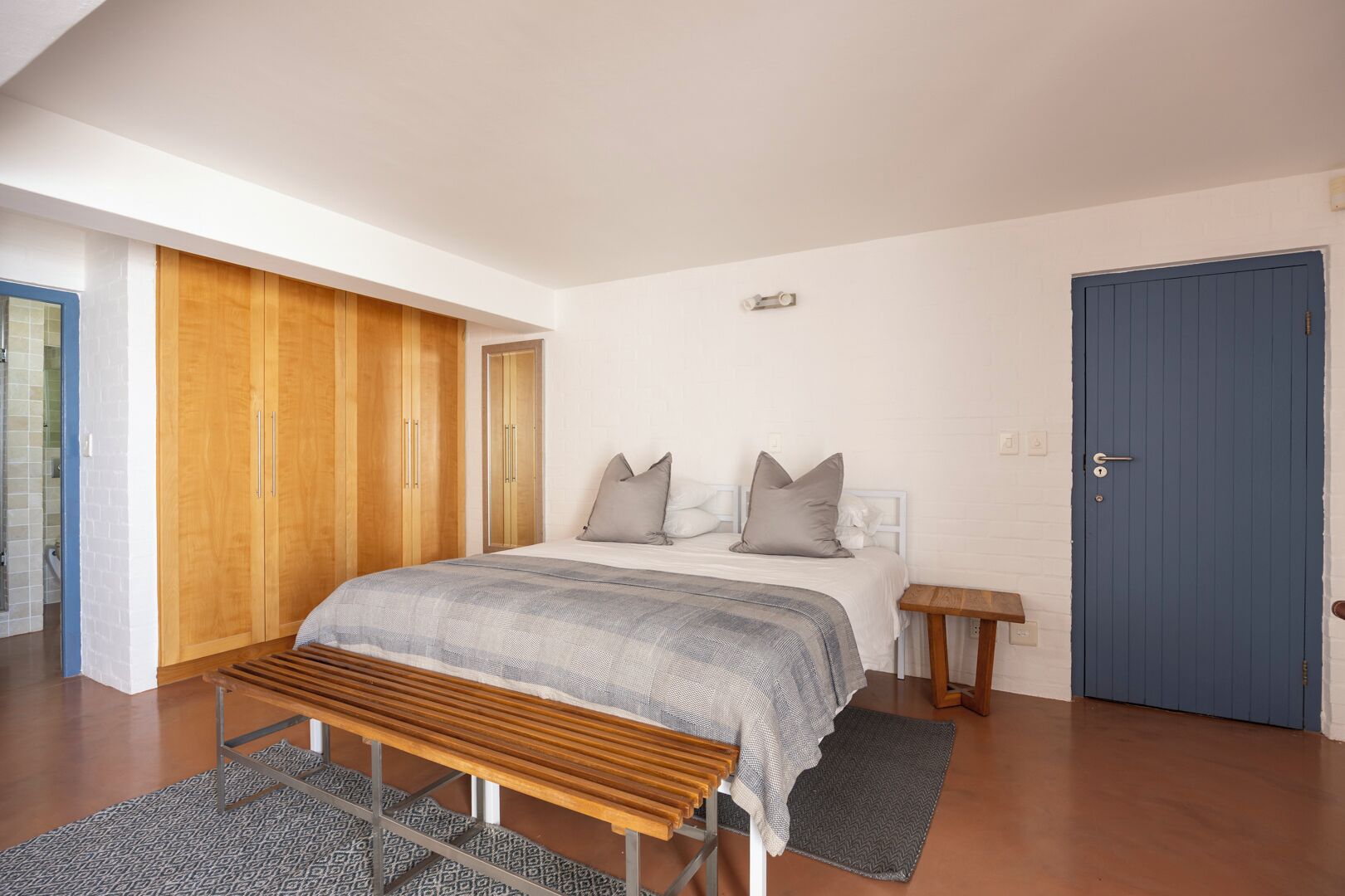 Ein Schlafzimmer mit Bett, Holzschrank, einer Bank, einem kleinen Tisch und einer blauen Tür.