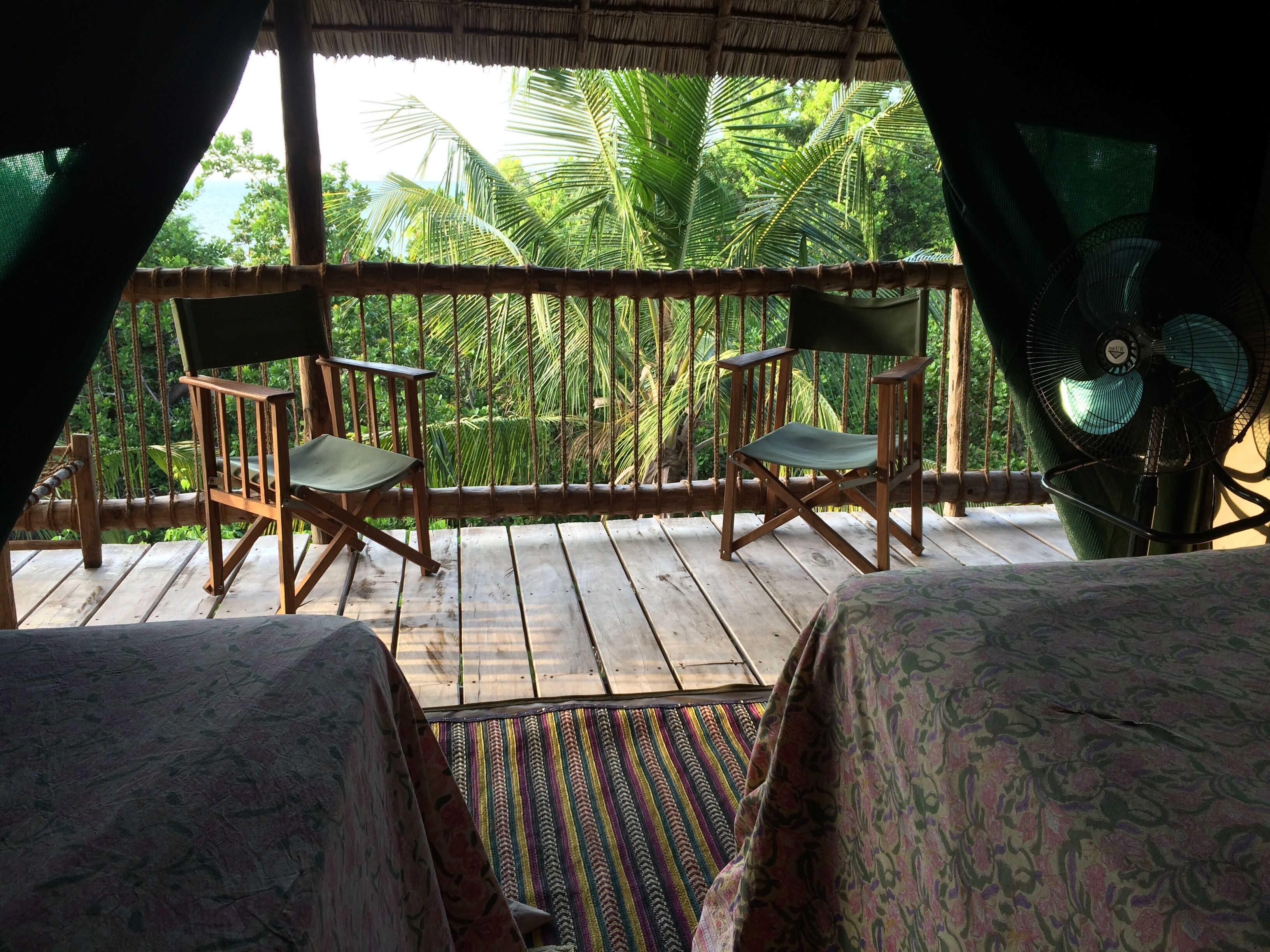 Une terrasse en bois avec deux chaises et une table en bois, offrant une vue sur un paysage verdoyant et luxuriant, parsemé de palmiers.