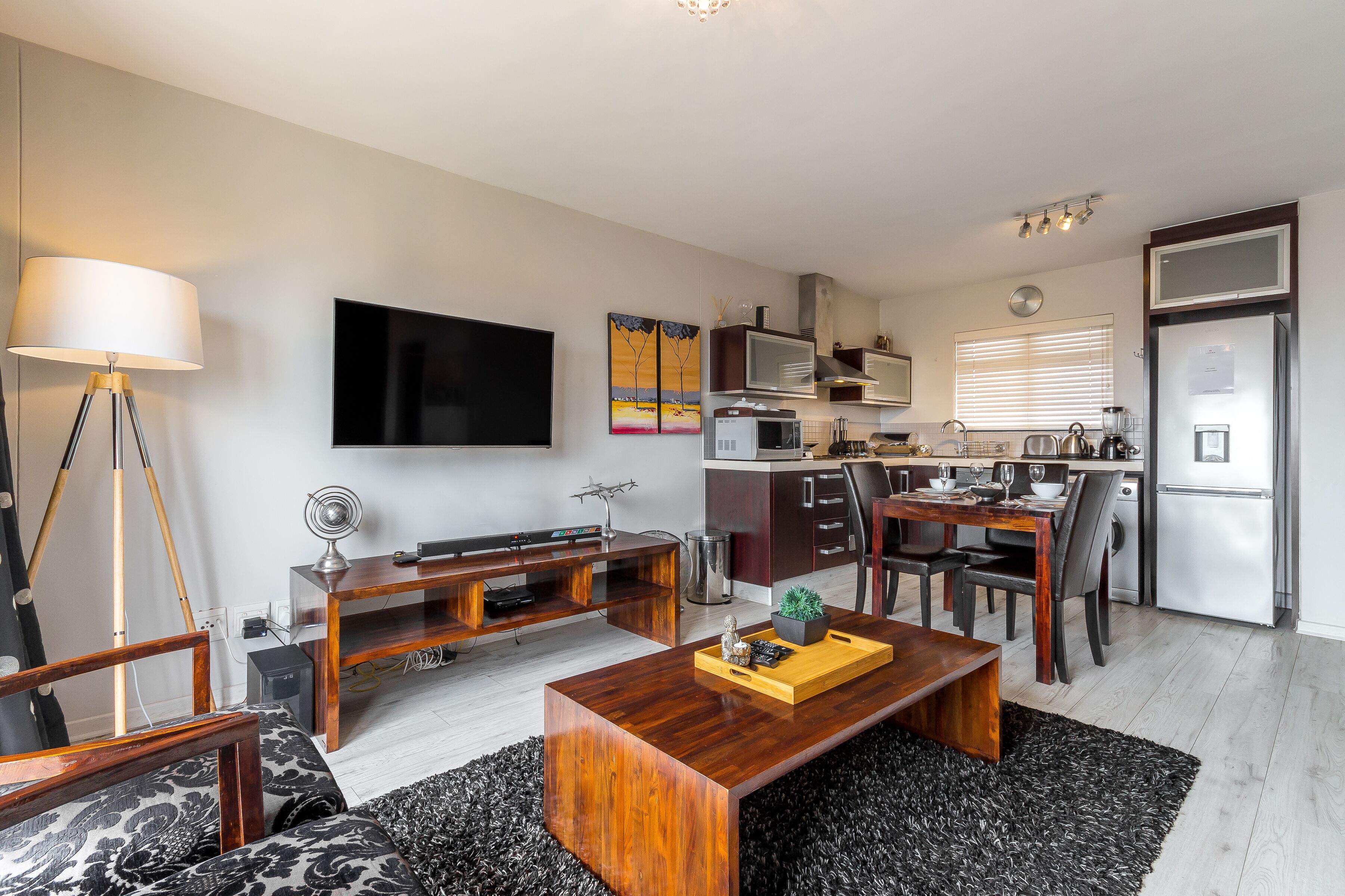 Een moderne woonkamer met een houten salontafel, een televisie en een eethoek, met een keuken op de achtergrond.