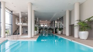 A large indoor swimming pool with a central staircase, surrounded by white pillars and potted plants. - Lavira (Cape Town)