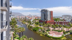 A riverside view of a modern urban area with high-rise buildings, palm trees, and a clear sky. - Lavira (Cape Town)