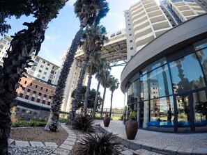 A modern building with a curved glass facade, surrounded by palm trees and a paved walkway. - Lavira (Cape Town)