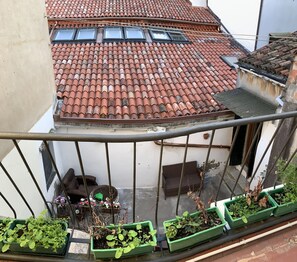 A balcony with green planters, a wicker sofa, and a tiled roof. - Royal Guest House Venice (Venice)