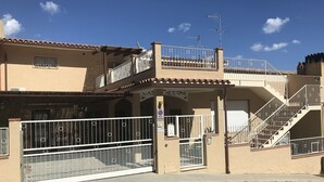A building with a gated entrance, a covered area with a sign, and a staircase leading to an upper level. - Casa Tacconi (Villasimius)