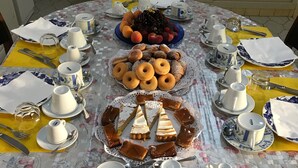 A round dining table set with various food items, plates, cups, and cutlery. - Casa Tacconi (Villasimius)