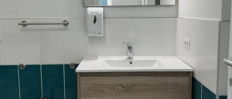 Ein Badezimmer mit Waschbecken in Weiß, einem Spiegel, einem Bidet und Fliesen in Türkis und Weiß.
