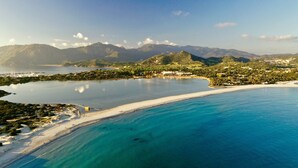 A coastal landscape with a beach, clear blue waters, and a mountainous backdrop. - Casa Tacconi (Villasimius)