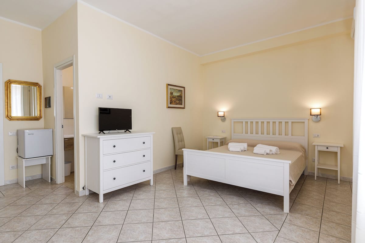A bedroom with a bed, a dresser, a television, and two bedside tables with lamps.