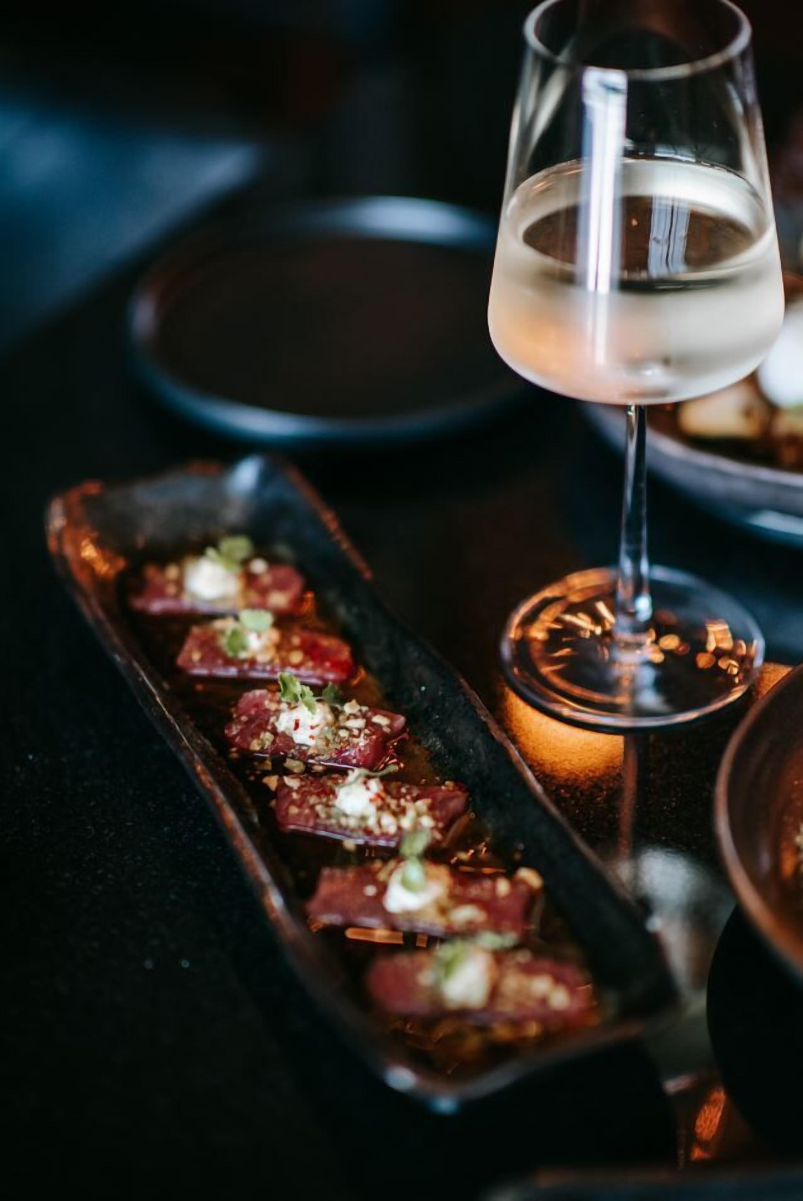 A dining table with a rectangular serving dish containing food, a glass of white wine, and a lit candle.