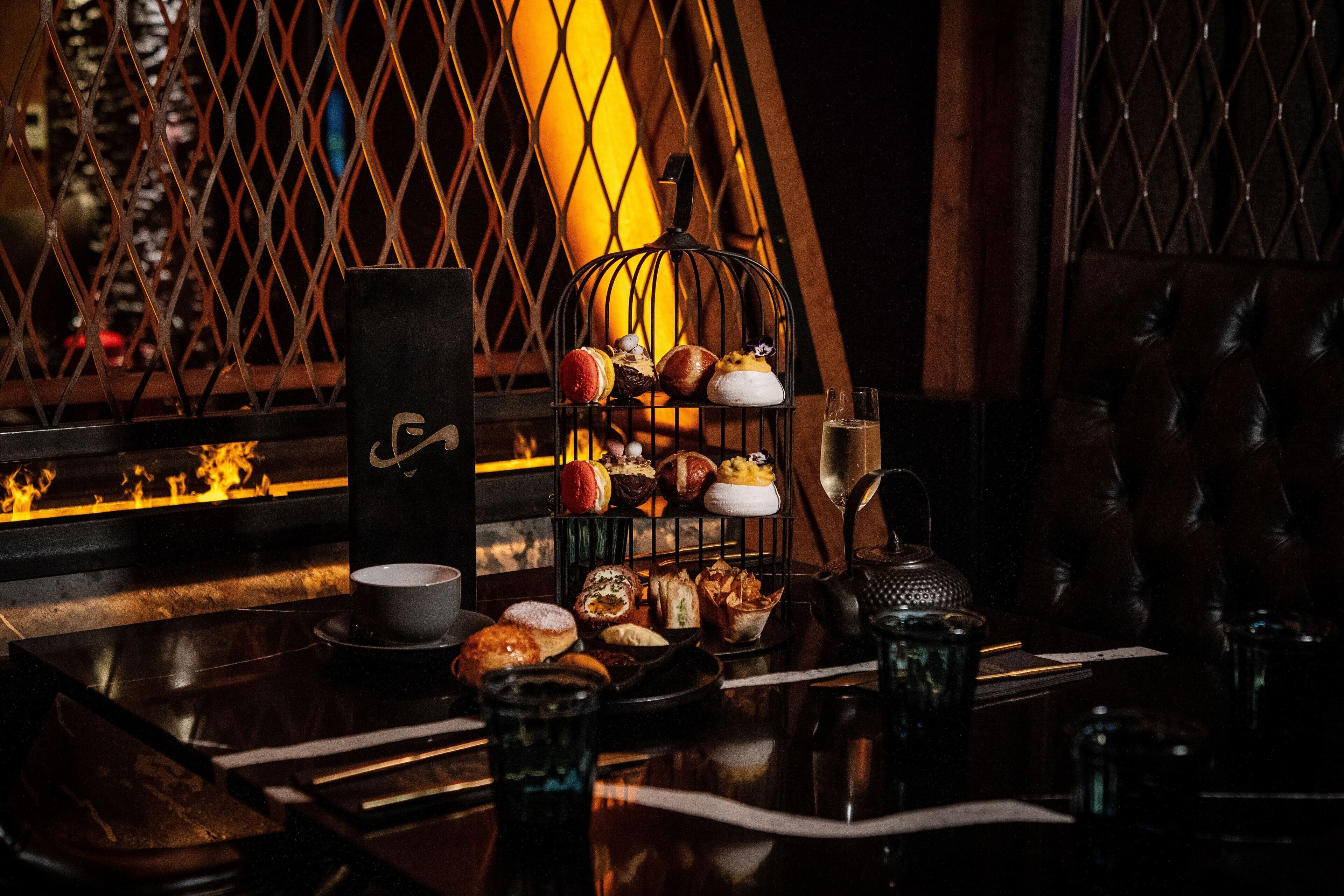 Une pièce faiblement éclairée, avec une table dressée pour un repas, où l’on peut voir une variété de pâtisseries et une bougie.