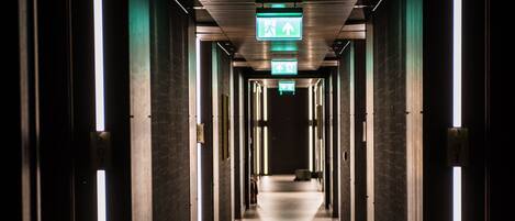 A long, narrow hallway with a series of doors on either side, illuminated by vertical light strips.
