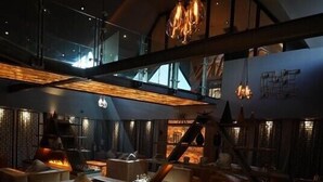 A modern lounge area with a fireplace, comfortable seating, and a high ceiling with exposed beams. - Cave Hotel & Golf Resort (Faversham)