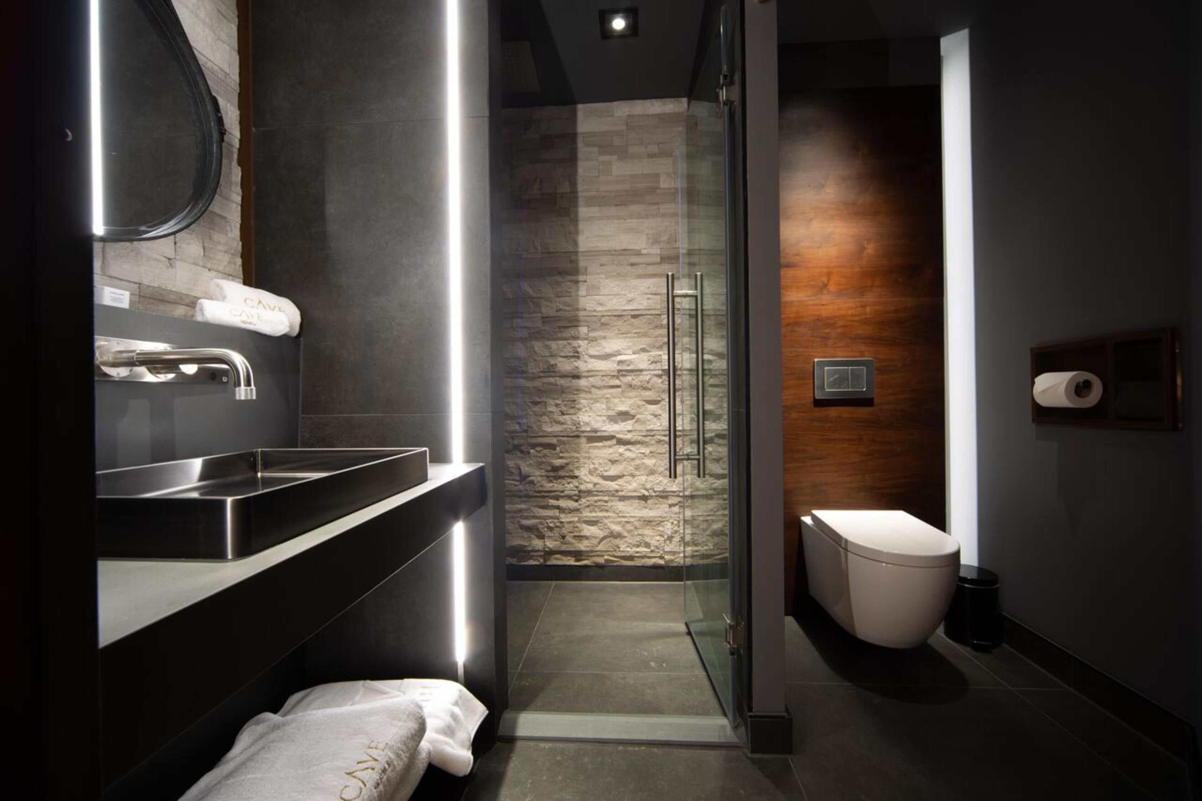 A modern bathroom with a stone wall, a glass shower enclosure, a white toilet, and a sink with a mirror.