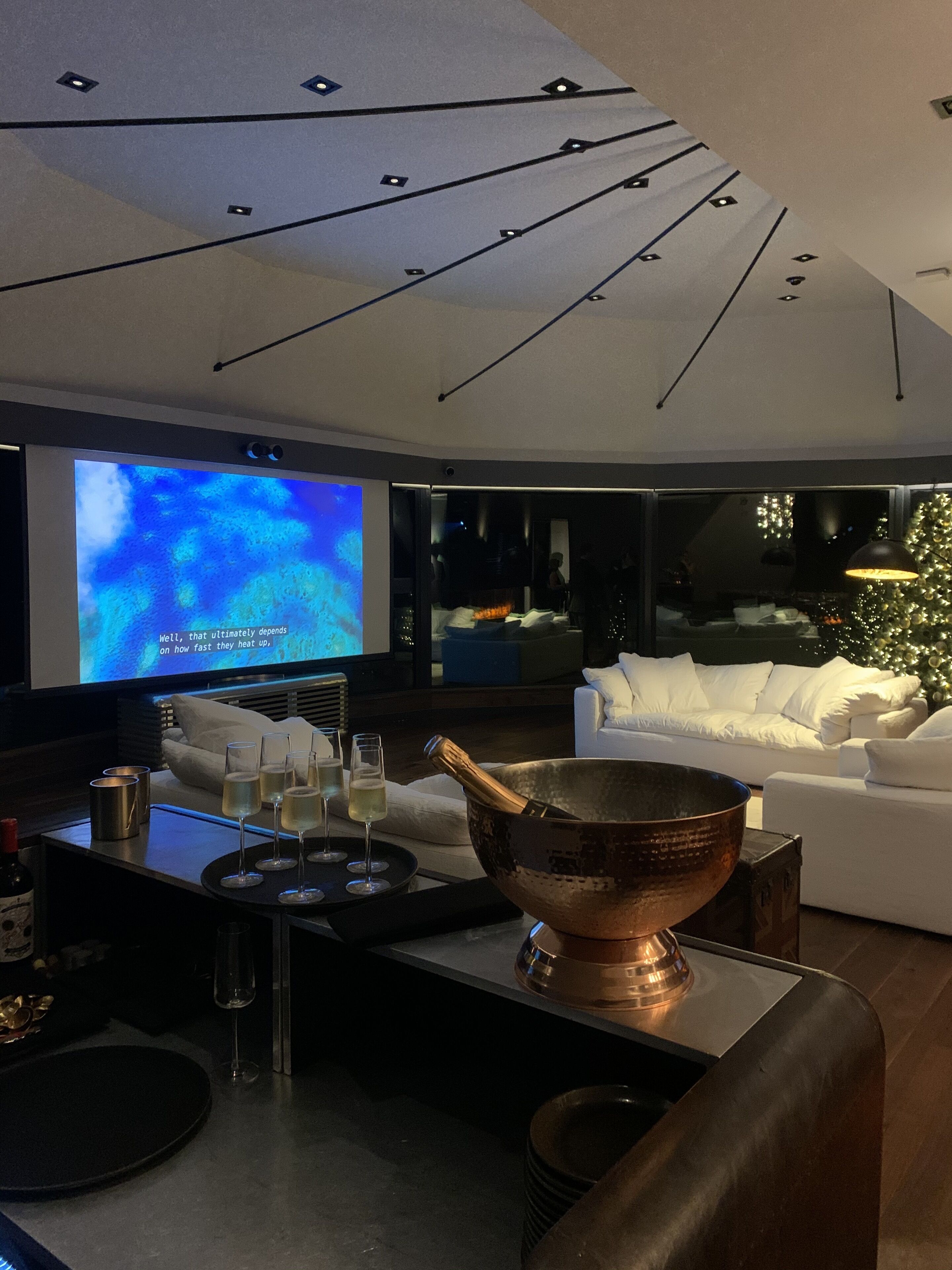 A modern living room with a large flat-screen TV, a white sofa, and a copper bowl on a table.