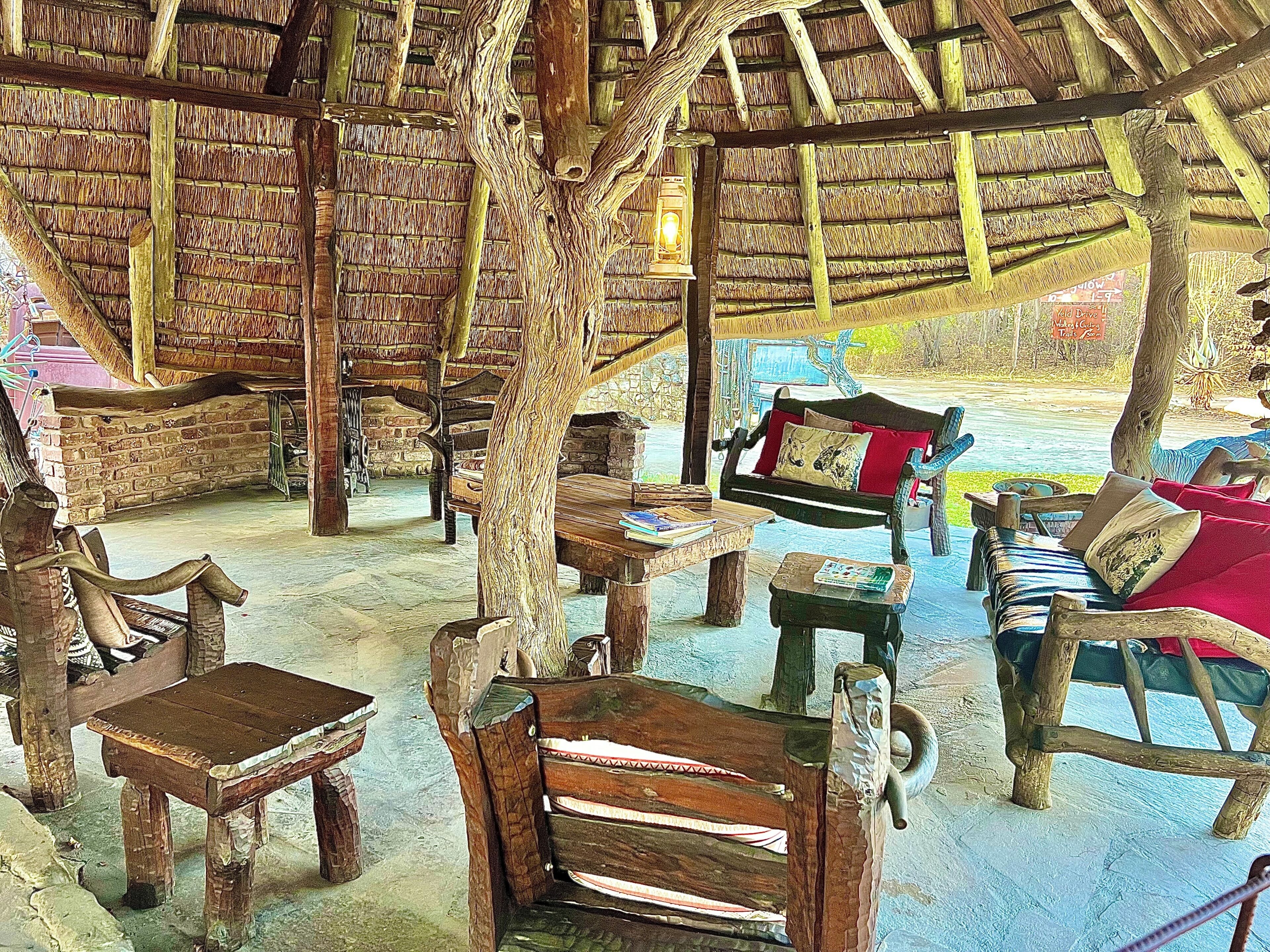 A rustic interior with wooden furniture, a thatched roof, and a stone wall.