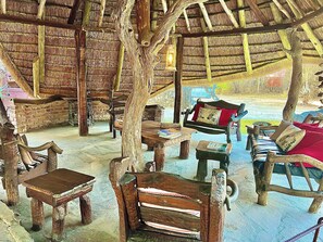 A rustic interior with wooden furniture, a thatched roof, and a stone wall.