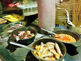 Variedad de platos de comida en cuencos y ollas, incluyendo salchichas, frijoles y otros ingredientes, sobre una mesa.
