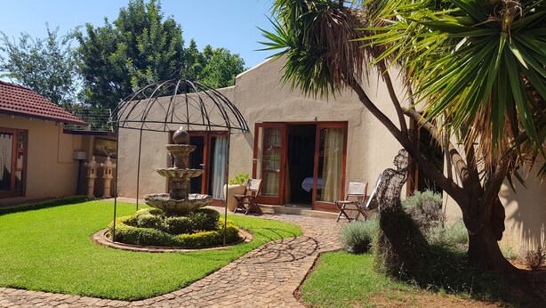 A courtyard with a stone fountain, a palm tree, and a building with a red-tiled roof. - Echo Garden Guesthouse (Rustenburg)