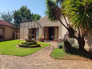 A courtyard with a stone fountain, a palm tree, and a building with a red-tiled roof. - Echo Garden Guesthouse (Rustenburg)