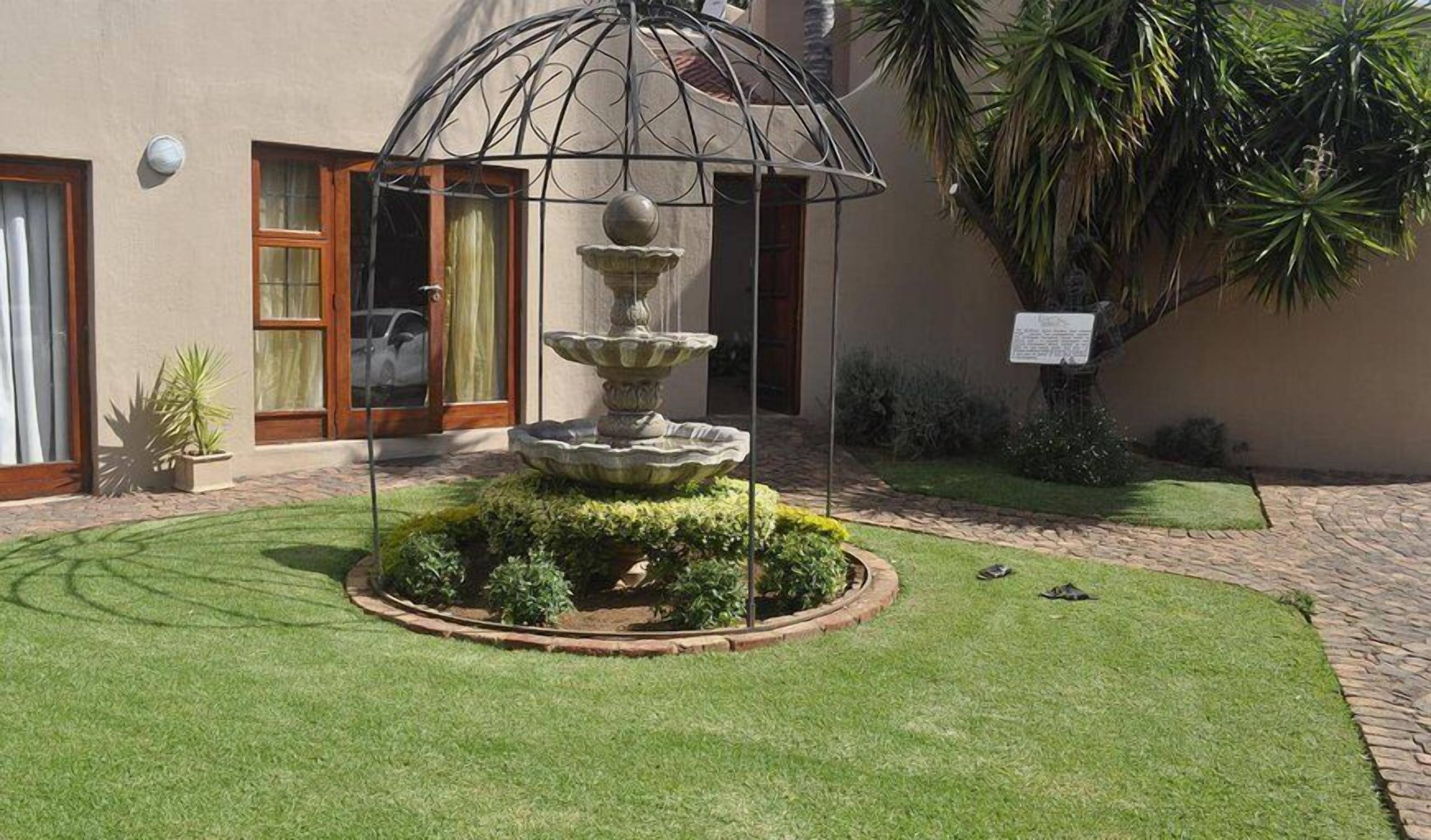 Une cour avec une fontaine à plusieurs niveaux, un palmier et un bâtiment doté d’une porte et de fenêtres.