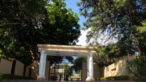 A gated entrance with a pergola, surrounded by trees and a paved pathway. - Echo Garden Guesthouse (Rustenburg)