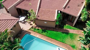 A residential property with a swimming pool, a patio with outdoor furniture, and a well-maintained lawn. - Echo Garden Guesthouse (Rustenburg)