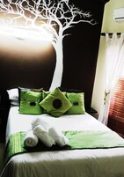 Una cama con ropa de cama verde, un mural de un árbol blanco en la pared y un aire acondicionado blanco.