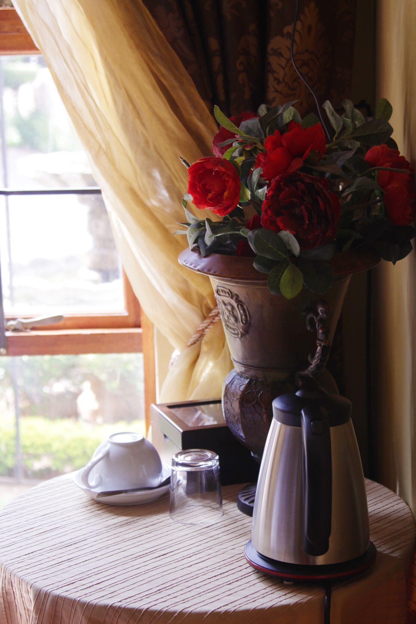 A table with a white teapot, a small glass, and a vase with red flowers.