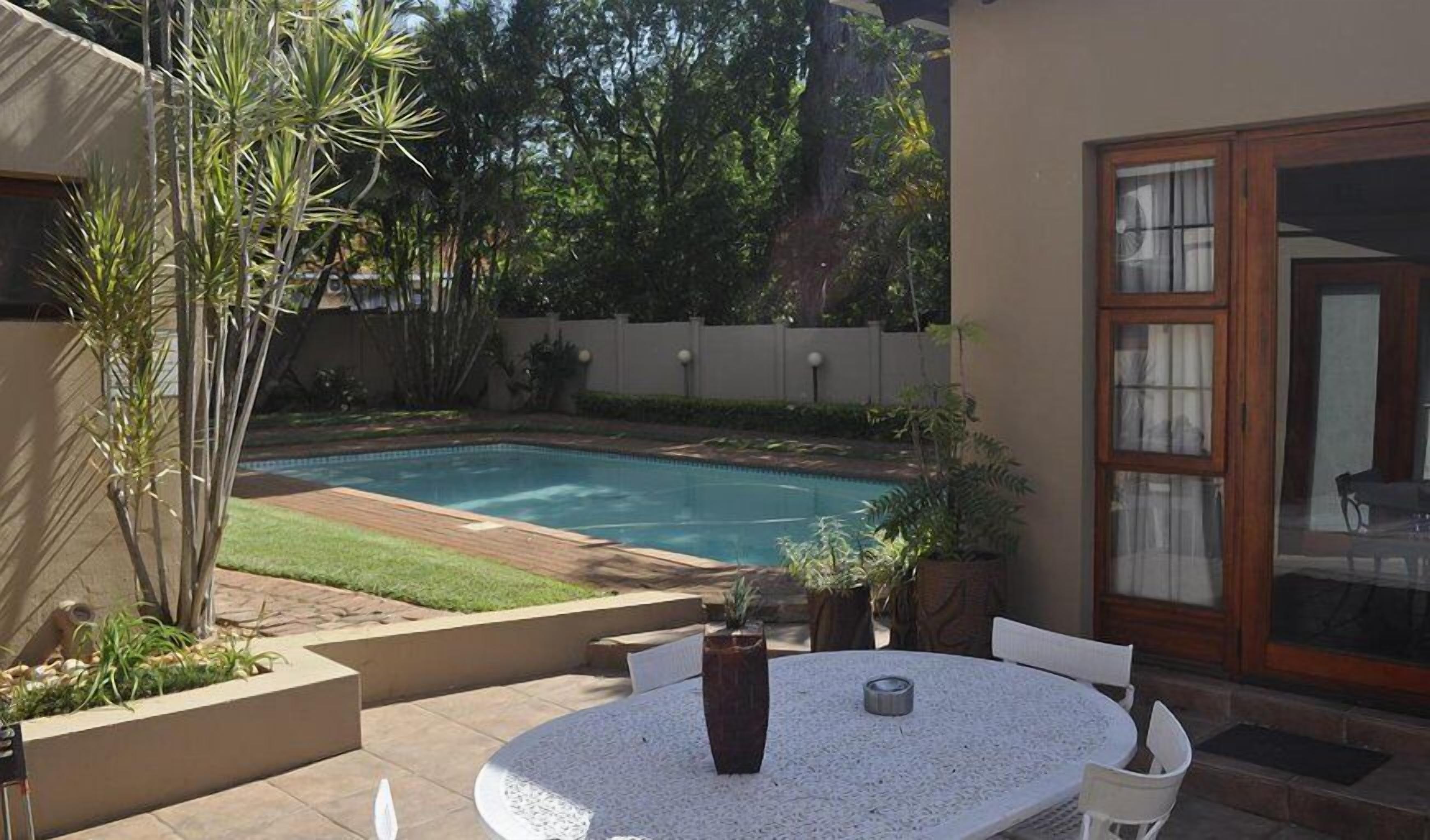 Un patio trasero con piscina, mesa y sillas.